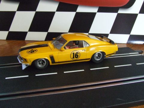 1973 Ford Mustang - A yellow 1970 Boss 302 Mustang slot car, number 16, races on a track with a checkered background.