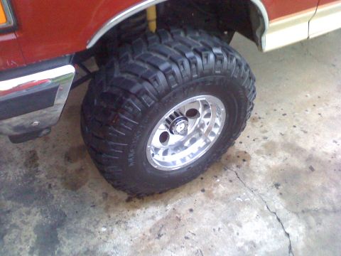 1990 Ford Bronco - A close-up shot focuses on a off-road tire and its polished alloy wheel, mounted on a vehicle.