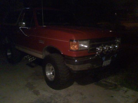 1990 Ford Bronco - This red pickup truck features a set of four off-road lights mounted on the front bumper.