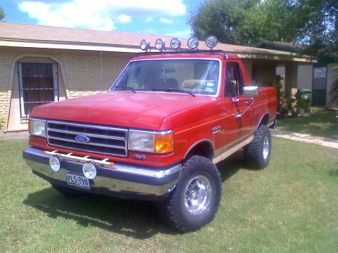 1990 Ford Bronco - This red Ford pickup truck features a lifted suspension and auxiliary lights on the roof rack.