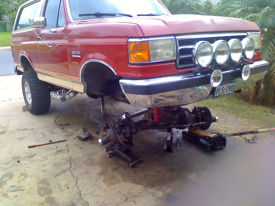 Red Ford Bronco on jack stands, front axle removed. License plate reads PLS 790