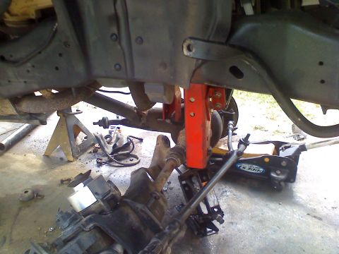1990 Ford Bronco - Vehicle undercarriage with suspension parts removed, supported by jack stands and a hydraulic jack.