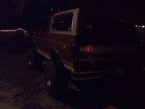 1990 Ford Bronco - Rear view of a red 1990 Ford Bronco with a white removable top, parked outdoors at night.