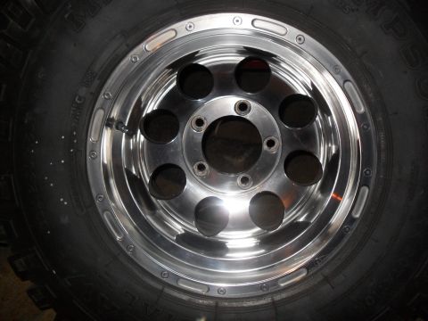 1990 Ford Bronco - Close-up of a chrome wheel and tire, a polished finish and six circular openings.