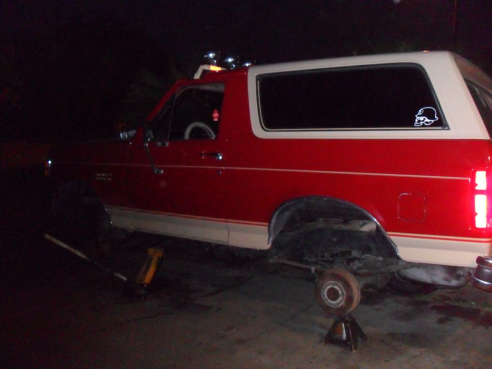 Side view of a red and tan 1990 Ford Bronco on jack stands