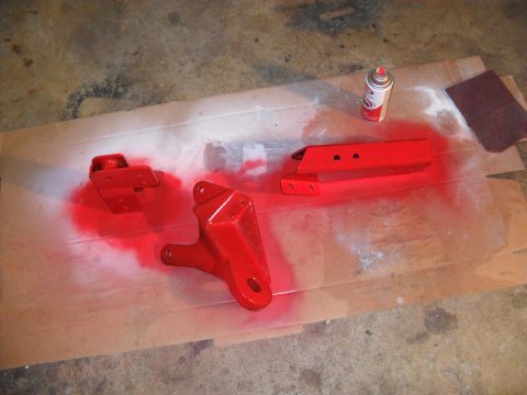 1990 Ford Bronco - Metal parts are spray painted red on cardboard, with a can of paint and sandpaper nearby.
