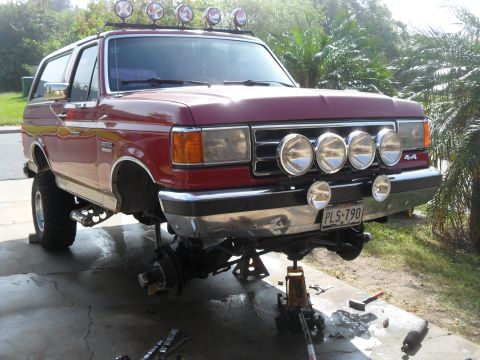1990 Ford Bronco - Red 1990 Ford Bronco undergoing front-end maintenance, lifted on jack stands.