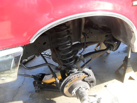 1990 Ford Bronco - Close-up of a red vehicle's front suspension system, showing components like the coil spring and brake assembly.