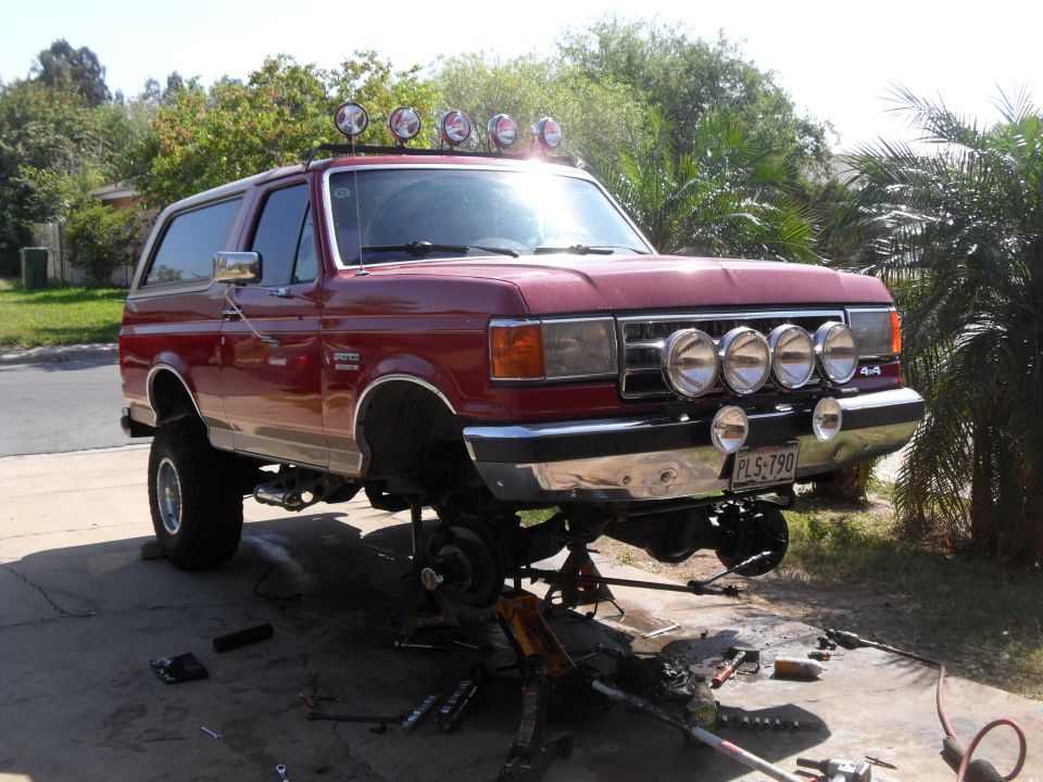 Red 1990 Ford Bronco with off-road lights, lifted, on jack stands