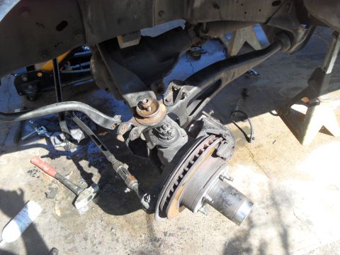 1990 Ford Bronco - The front suspension and brake assembly of a vehicle is shown disassembled, with tools nearby.