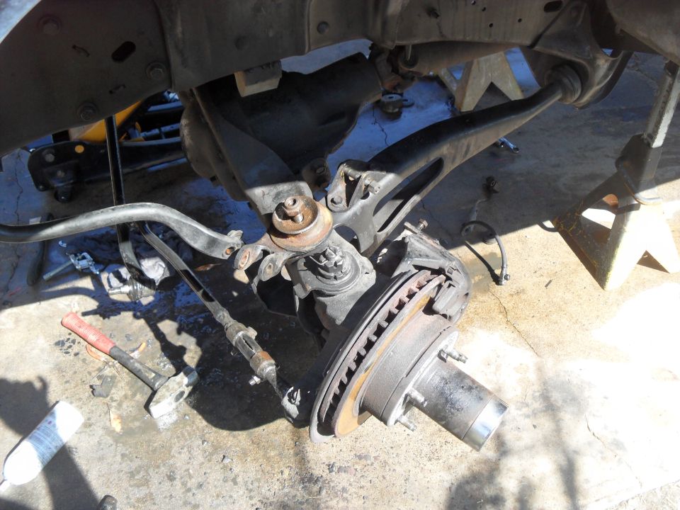 close-up of vehicle's front suspension and brake components, with tools on the ground