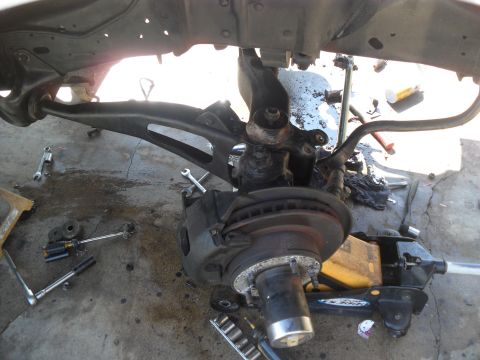 1990 Ford Bronco - Close-up view of a vehicle's front suspension and brake components, with tools scattered around.