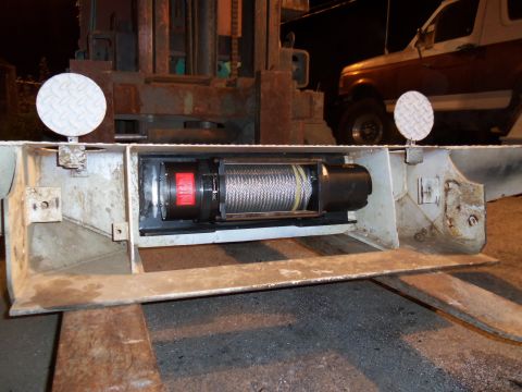 1989 Ford Bronco - A winch mechanism is visible on a trailer, with a forklift and a truck in the background.