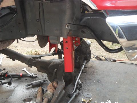 1990 Ford Bronco - Close-up view of red vehicle frame and suspension components, with tools scattered on the ground.