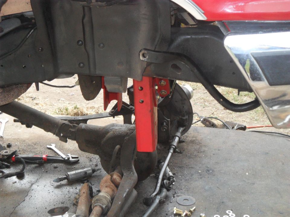 Red vehicle frame with suspension parts and tools on the ground
