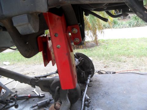 1990 Ford Bronco - Close-up of a red suspension component being worked on, with the vehicle's axle and brake assembly visible.