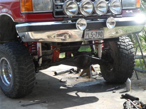 1990 Ford Bronco - Front view of a red lifted truck with large off-road tires and multiple spotlights mounted above the bumper.