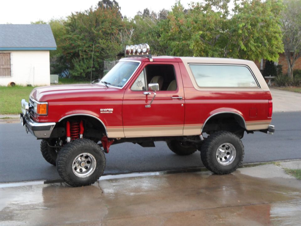 Lifted red Bronco with tan top, off-road tires, and light bar on roof