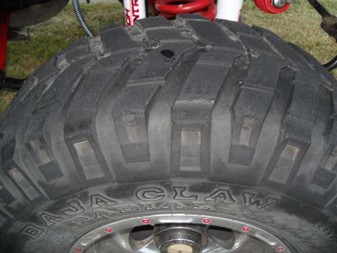 1990 Ford Bronco - Close-up of a tire with "BAJA CLAW RADIAL" text and visible suspension components.