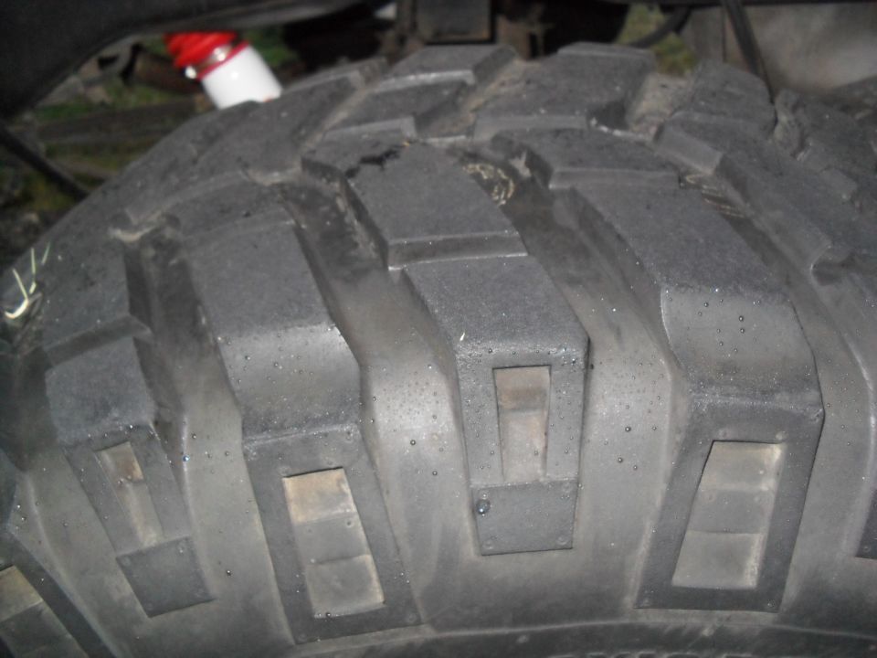 Close-up of a knobby off-road tire tread. Red and white shock absorber visible above