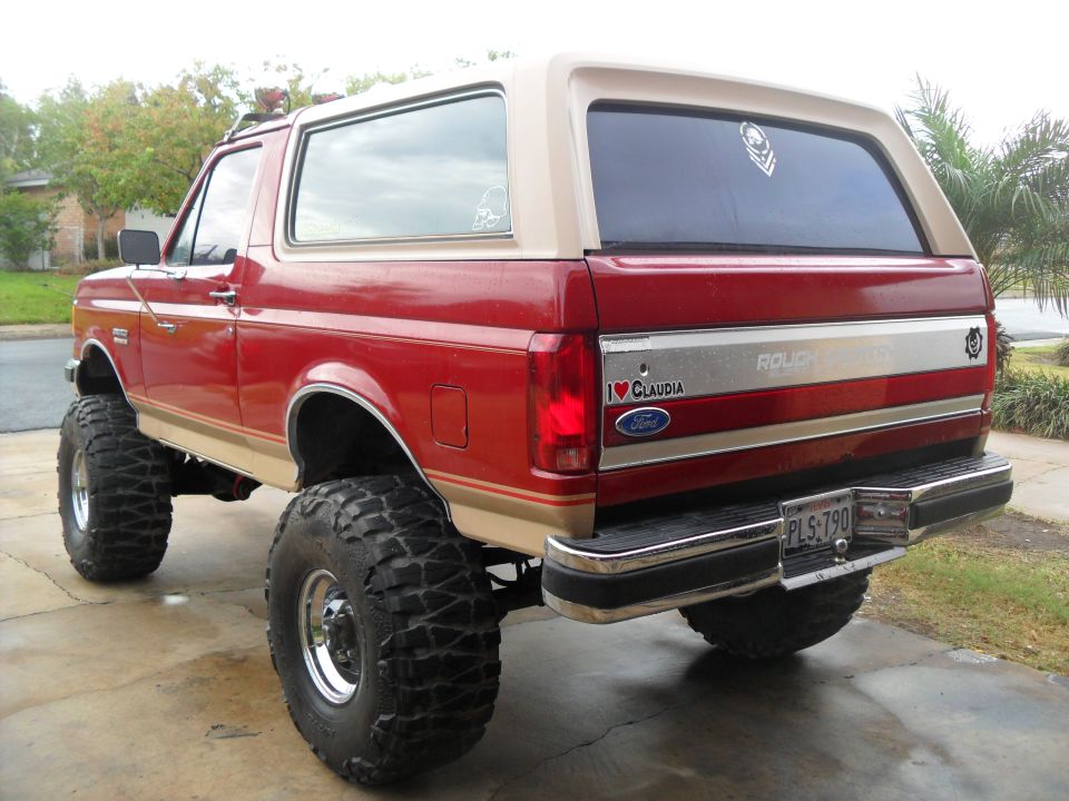 Red and tan 1990 Ford Bronco with lifted suspension and large off-road tires, viewed from the rear