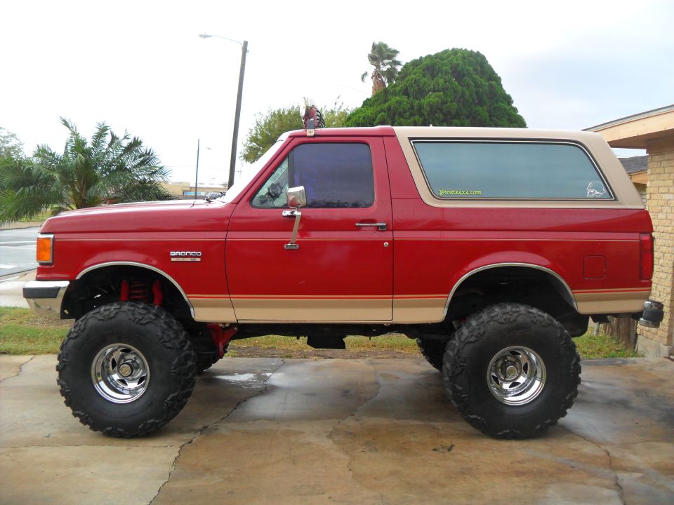 Red 1990 Ford Bronco side view with lifted suspension and large tires