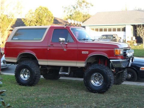 1990 Ford Bronco - This lifted 1990 Ford Bronco features a two-tone red and tan paint scheme and prominent off-road tires.