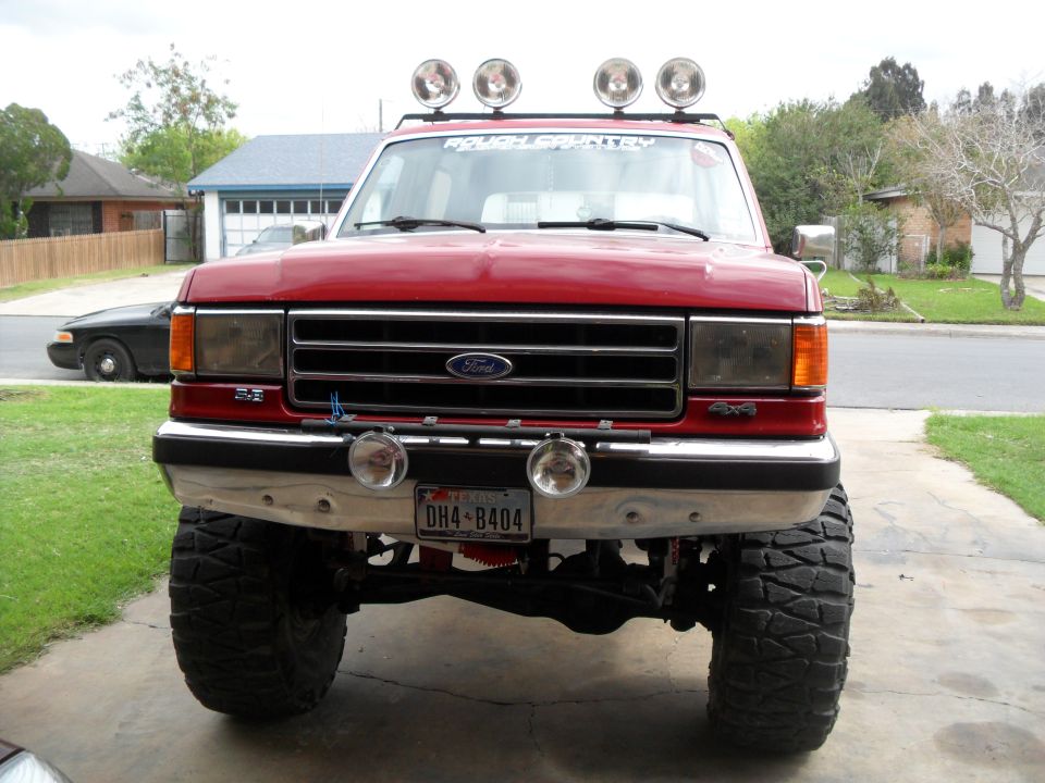 Red Ford F-Series truck with lifted suspension and off-road tires, front view
