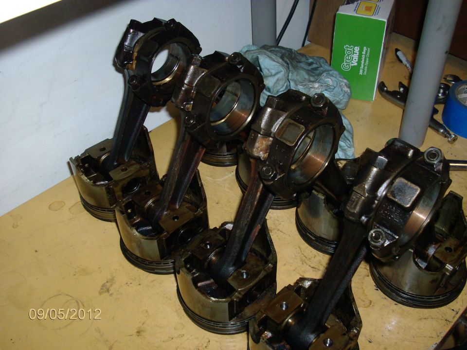 Several engine pistons with connecting rods attached, laid out on a table