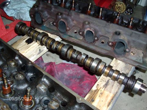 1979 Ford F-150 - A used V8 camshaft rests on scrap wood blocks across a workbench, its lobes and bearing journals showing brown heat and oil staining and a…