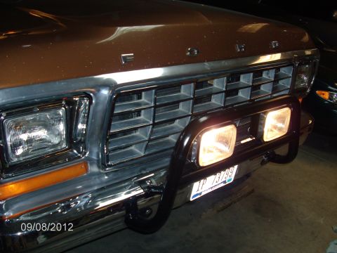 1979 Ford F-150 - Close-up night shot of the front end of a brown Ford pickup, showing the chrome-trimmed egg-crate grille with raised FORD hood lettering, r…
