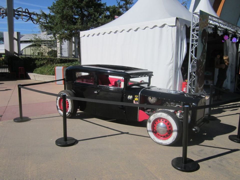 Black hot rod with red interior and white-wall tires, parked behind stanchions