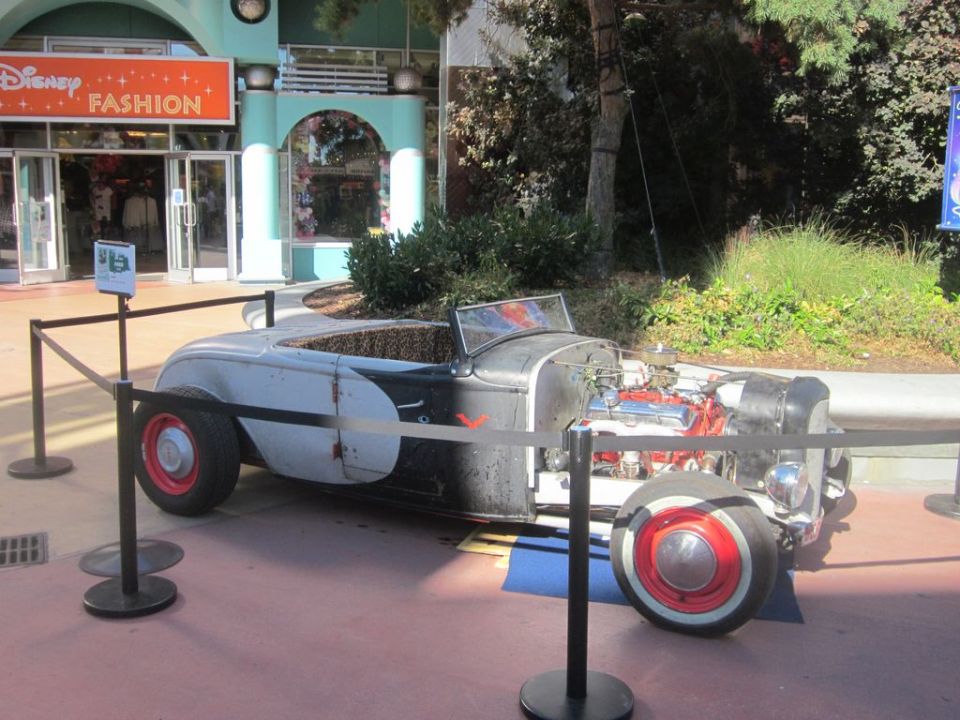 Hot rod with exposed engine and red wheels parked outside a Disney store