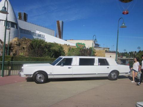1991 Ford LTD Crown Victoria - A white stretch limousine is parked outdoors on a sunny day with a building and a hot air balloon visible.