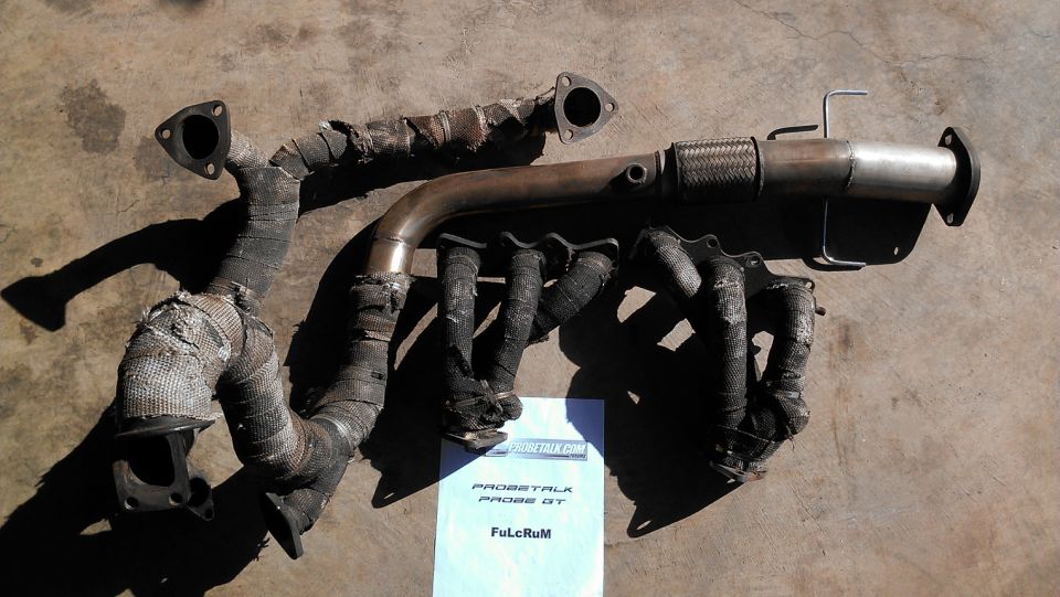Heat-wrapped tubular exhaust headers and stainless flex downpipe on concrete with a ProbeTalk sale sheet