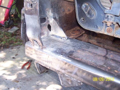 1990 Ford Bronco - Close-up of a vehicle's frame and bumper undergoing repair, with a pair of pliers visible on the concrete.