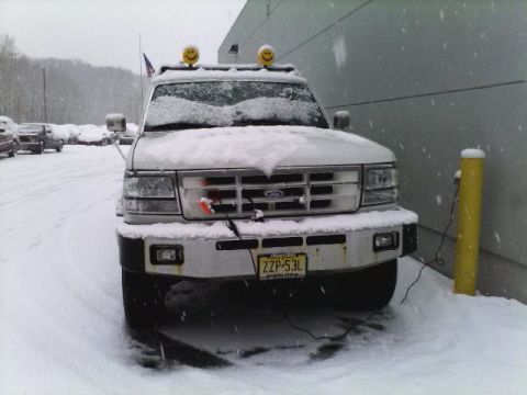 1994 Ford C-350 (Centurion Conversions) - A snow-covered Ford truck is parked outside in a winter storm, with electrical cords running to it.