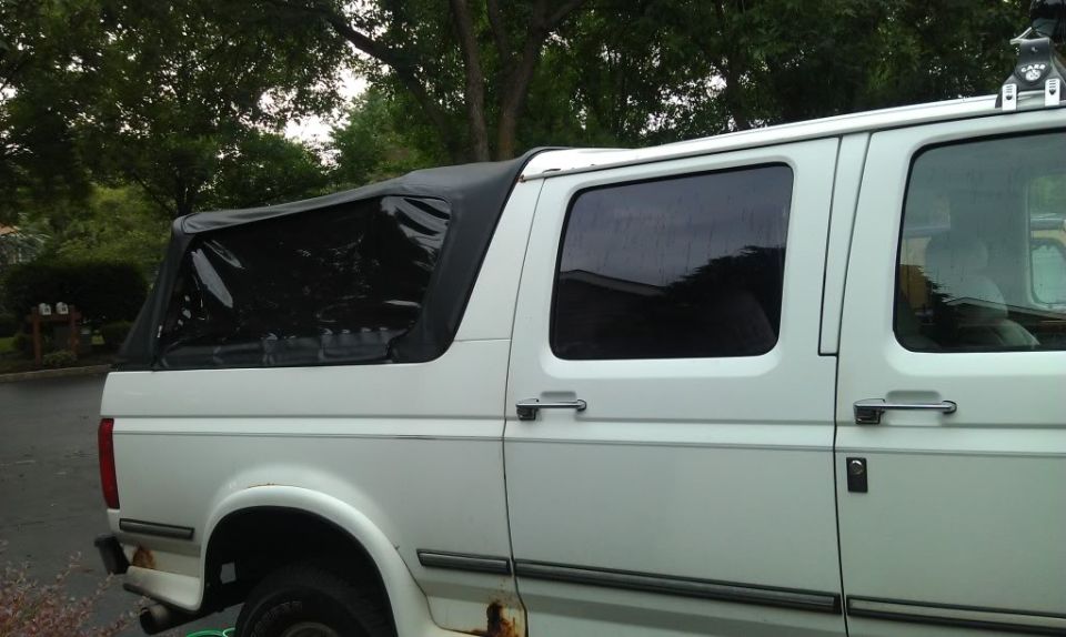 Side view of a white van with a black soft top covering the rear cargo area. Rust is visible on the lower body panels