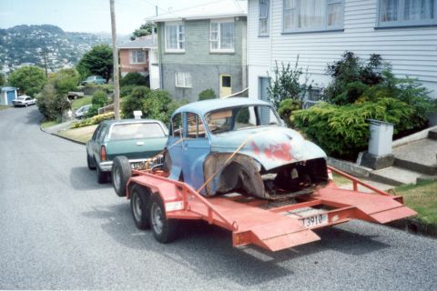 1969 MINI Cooper - A blue car body, missing its front end, is transported on a trailer behind a green SUV.