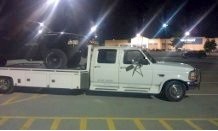 1979 Ford Bronco - Flatbed truck carrying a black SUV in a parking lot after dark.