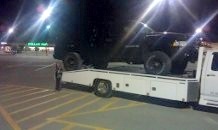 1979 Ford Bronco - A black SUV is loaded onto a tow truck in a dimly lit parking lot at night.