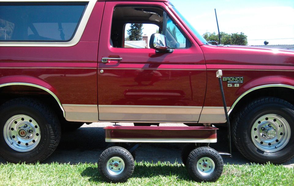 Side view of burgundy and tan Ford Bronco with 5.8 badge and steel wheels, small matching model below