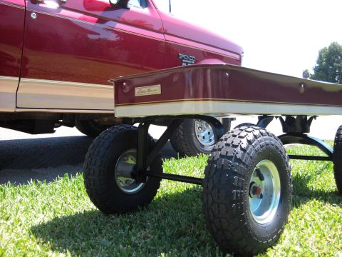 1994 Ford Bronco - Ground-level view of a custom burgundy-and-tan pull wagon with a gold "Eddie Bauer" nameplate and pinstripe, riding on four knobby turf tir…