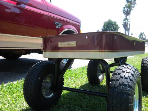 1994 Ford Bronco - Low-angle shot of a custom two-tone burgundy-and-tan pull wagon badged "Eddie Bauer," sitting on knobby turf tires in the grass and painted…