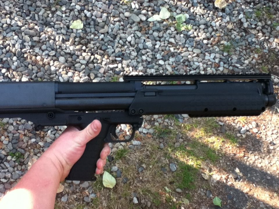 Black bullpup shotgun held by a hand over a gravel surface outdoors