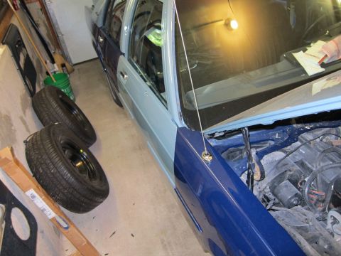 1991 Ford LTD Crown Victoria - A car undergoing work in a garage, with its hood open and spare tires nearby.