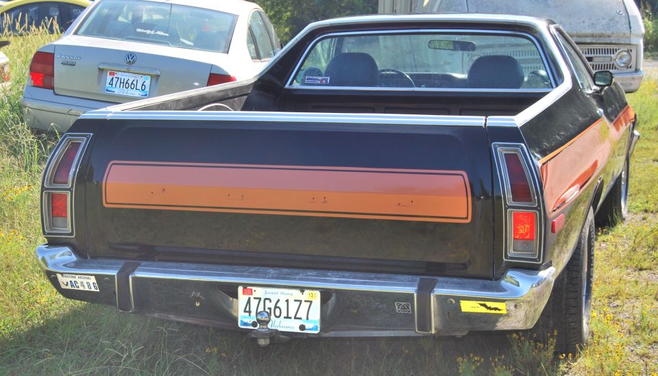 1975 Ford Ranchero rear view, black with orange stripe. Another car and van visible