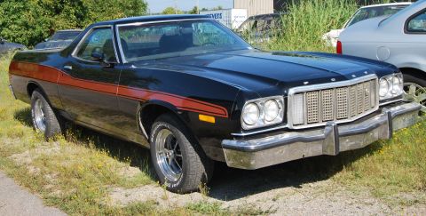 1975 Ford Ranchero - A black 1975 Ford Ranchero with distinctive orange side stripes is shown from a three-quarter front angle.