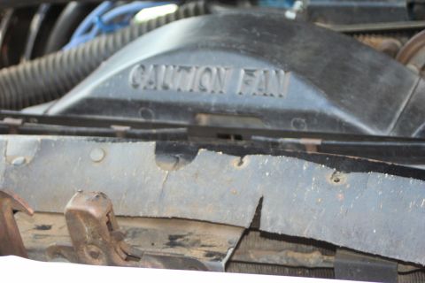 1976 Ford Ranchero - Close-up of an engine fan shroud with warning text. The surrounding area shows signs of wear and tear.