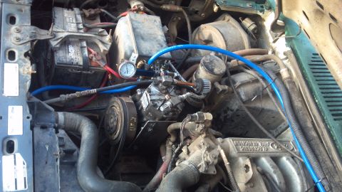 1986 Ford Bronco - Close-up view of a vehicle's engine bay, showing the AC compressor and a pressure gauge.